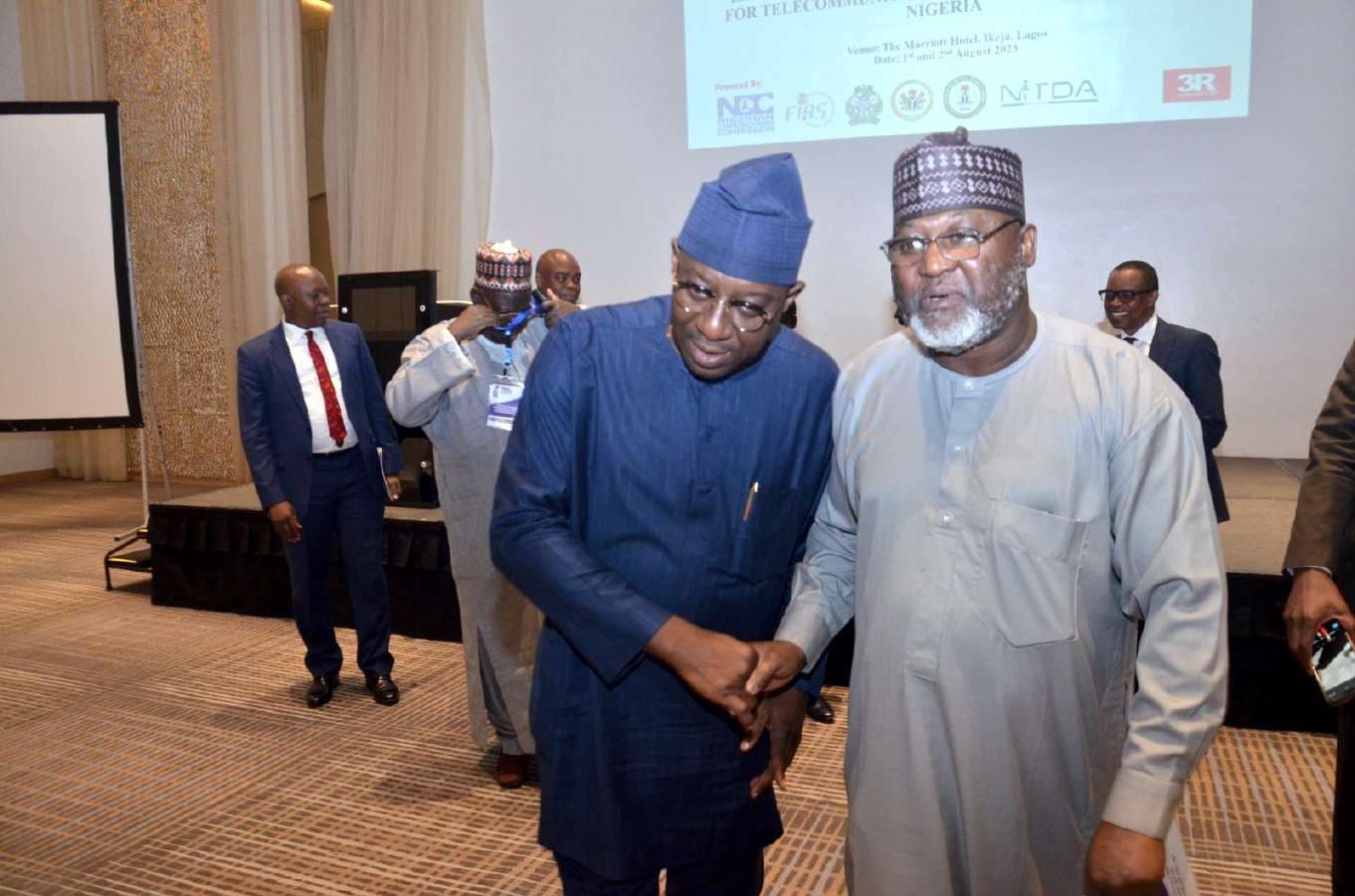 Delegates shaking hands in front of the workshop step-and-repeat banner listing NCC, FIRS, ICRC, ONSA, NITDA and 3R Consortium